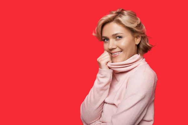 Retrato de cerca de una mujer sonriente en suéter mirando a la cámara aislada sobre fondo rosa con espacio de copia. — Foto de Stock