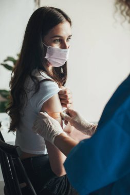 Doctors hands puts plaster over place of vaccination against coronavirus to a patient wearing a face mask.