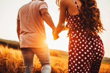 Couple walking along the wheat field holding hands on a sunny day. Light backdrop. Wheat field.