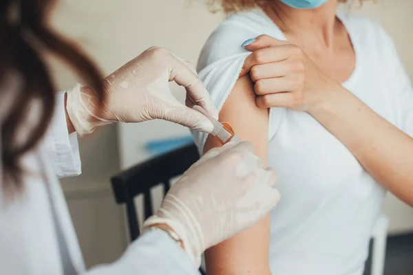 Closeup portrait of a doctor hands putting a plaster at female arm after injection of a corona virus vaccine. Medical treatment. — Stock Photo, Image