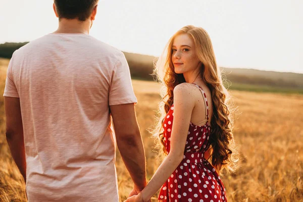 Couple holding hands in a wheat field. Woman looking back. Sunset — 图库照片