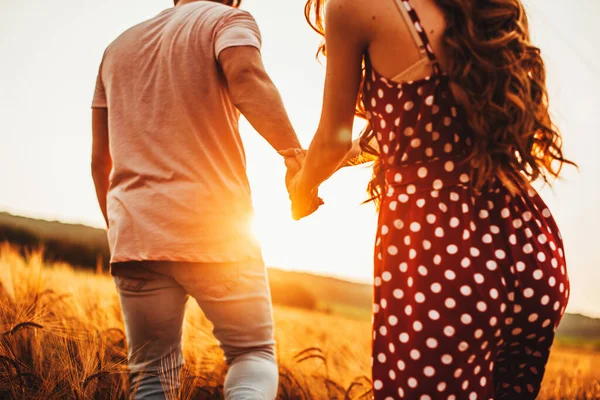 Couple walking along the wheat field holding hands on a sunny day. Light backdrop. Wheat field. — Stockfoto