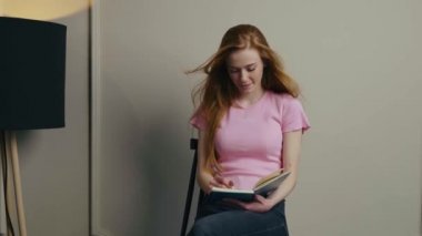 Red haired woman writing down notes while sitting on chair isolated over white wall. Businesswoman portrait. Writing education concept. Home concept. Workplace