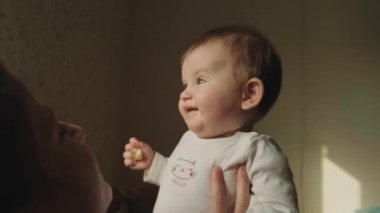 Mohers hands holding her baby girl while they sitting on the bed. Family care. Baby care.