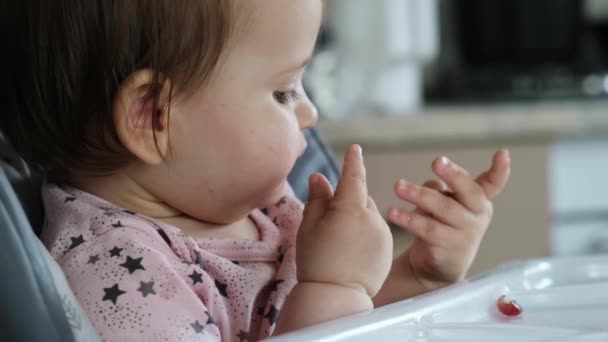 A kislány gránátalmát eszik egy etetőszékben otthon. Gyönyörű portré. Vegetáriánus egészséges étel. Friss egészséges étel. Bioélelmiszerek. — Stock videók