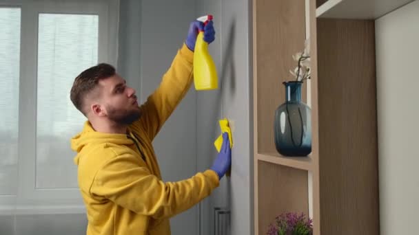 Hombre caucásico está limpiando su habitación con guantes y limpiando con aerosol antiséptico — Vídeos de Stock