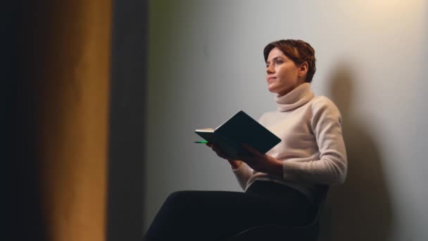 Adorable woman with short hair is reading from a book and speaking during an online meeting — 图库视频影像