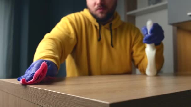 Bearded houseworker is cleaning the house using a wipe and disinfectant spray while wearing gloves — ストック動画