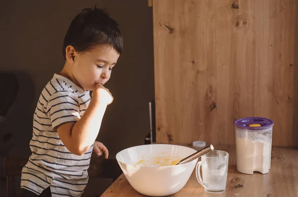 Мальчик пробует тесто, приготовленное его матерью. Сладкая еда. — стоковое фото