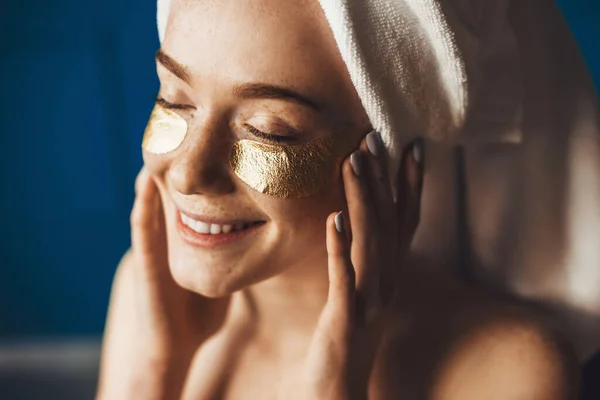 Close-up portret van een sproeten vrouw met handdoek op het hoofd gebruik maken van gezicht gouden ooglapje voor de huid. Schoonheidsbehandeling. Schoonheidsmode model. Schoonheidsgezicht — Stockfoto