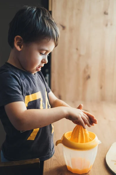 Side view of a boy making fresh orange juice by automatic juicer for the breakfast. Boy squeeze orange for lifestyle design. Organic tropical fruit juice. — Φωτογραφία Αρχείου