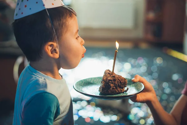 Close-up portrait of a little boy blowing out the candles on the piece of cake given by mom. Sweet food. Holiday celebration. Birthday party. — Fotografia de Stock