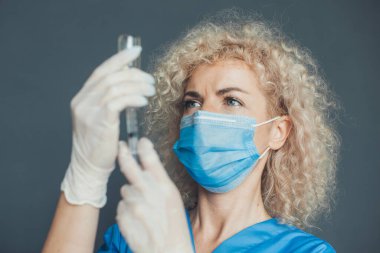 Tıbbi eldivenli ve maskeli bir kadın doktorun yakın plan portresi. Elinde şırıngayla hastanede. Coronavirus aşısı. El ele tutuşarak. Tıbbi