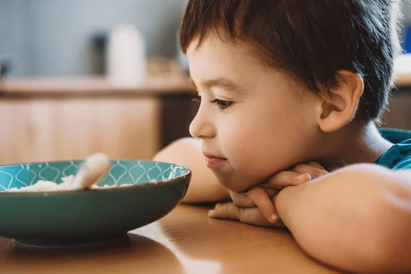 Boy with his head resting on the table and wondering whether to eat the porridge or not. — Fotografia de Stock