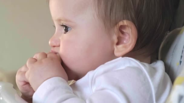 Baby girl sitting on high children chair holding and eating a piece of banana. Great design for any purposes. — Video Stock