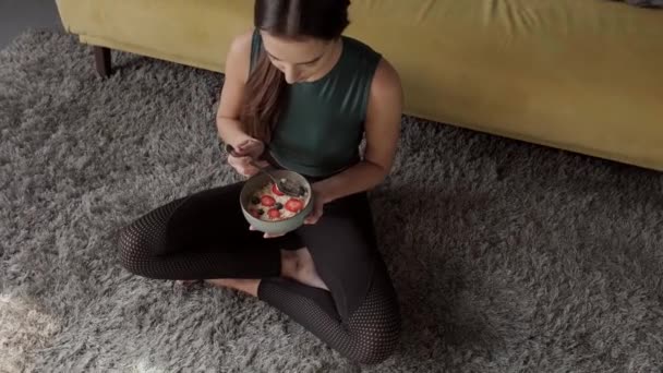Woman eating a bowl of nutritious oatmeal sitting on floor. Healthy food, diet. Healthy lifestyle. Body care. — Stok video
