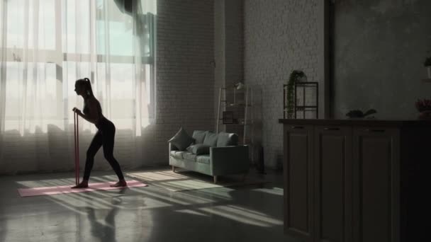 Distant view of a woman doing exercises with resistance bands at home. Girl doing yoga. — 图库视频影像