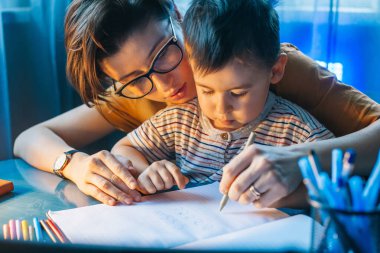 Little boy doing homework at home with school books helped by his mother. For lifestyle design. Family care. Children education. Family day.