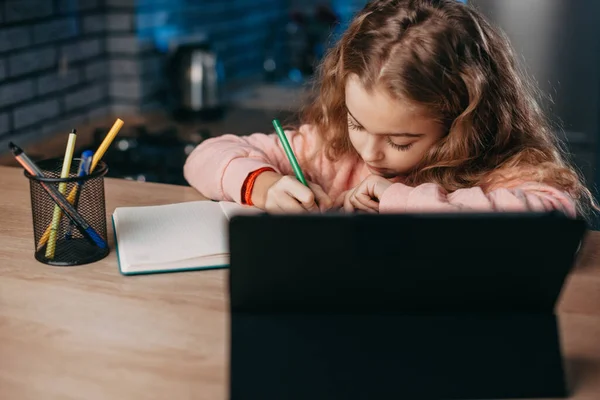 Niña estudiando y tomando notas usando una tableta digital mientras está sentada en casa. —  Fotos de Stock