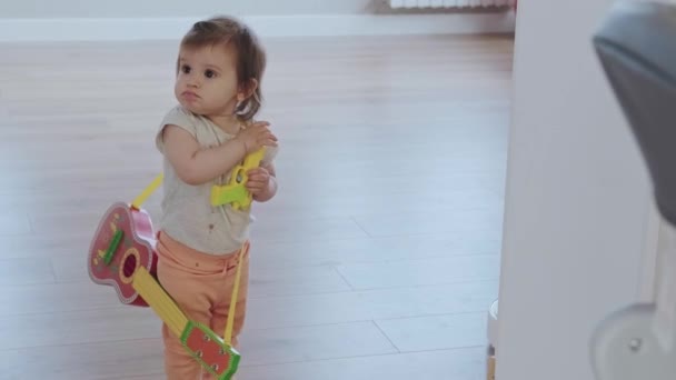 Video with a baby girl standing with a toy gun and a guitar. Beautiful young girl. — Stockvideo
