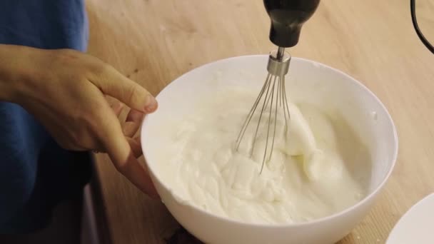 Video met handen mengen witte ei crème in kom met motor mixer. — Stockvideo