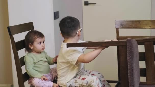 Відео з двома кумедними маленькими братами і сестрою робить вигляд, що керує уявною машиною на стільці. Творча концепція. Щаслива концепція дитинства. Сімейна концепція — стокове відео