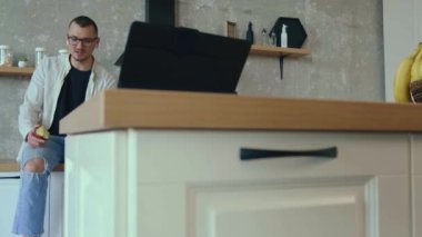 Evdeki mutfakta oturmuş elma yerken telefonda konuşan beyaz, gülümseyen bir adam. Konuşan insanlar. Akıllı ev. Mobil iletişim.