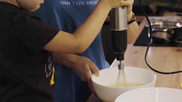 Video di una mamma che tiene un mixer e mostra al figlio come impastare la pasta. Concetto stile di vita familiare. Concetto di cibo. Concetto infanzia felice. Concetto casa. — Video Stock