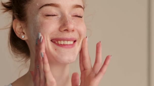 Video of a caucasian freckled woman applying anti-aging cream on her face. Smiling face. Woman applying cream face, great design for any purposes. Natural — Stock Video