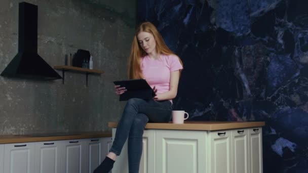 Video de una mujer sentada en la mesa de la cocina y buscando recetas en internet en la tableta — Vídeo de stock