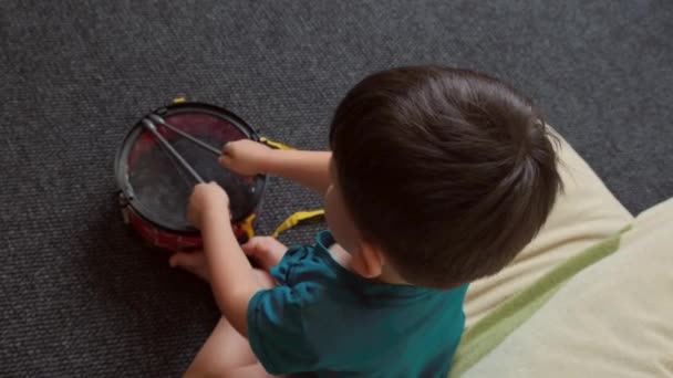 Vidéo. Vue du dessus d'un garçon battant des mains après avoir joué de la batterie assis dans la pièce. Garçon après avoir joué du batteur — Video