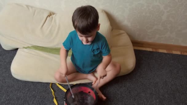 Video med en dreng sidder på gulvet og spiller legetøjstromme, i sidste ende klapper sig selv. Børneudvikling. – Stock-video