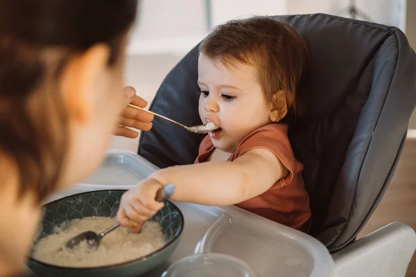 Bebê sentado em cadeira alta sendo alimentado por mães mãos. Para design de estilo de vida. Alimentos saudáveis. — Fotografia de Stock