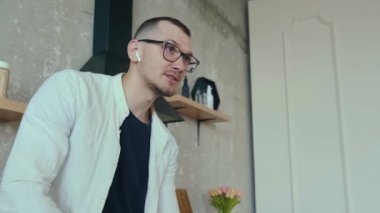 Mutfak masasında oturan ve telefonla konuşan bluetooth 'la bağlanan ve elma yiyen bir adamın videosu. Çevrimiçi iletişim.