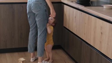 Bebek tezgahı olan ve annesinin bacaklarını tutarak onu kollarına alması için yalvaran bir video. Aile koruması. Bebek bakımı. El ele tutuşarak.