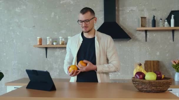 Mutfakta iki portakalla hokkabazlık yaparken bir iş adamının tabletle video görüşmesi. İnternetteki konferans. İnternet teknolojisi. — Stok video