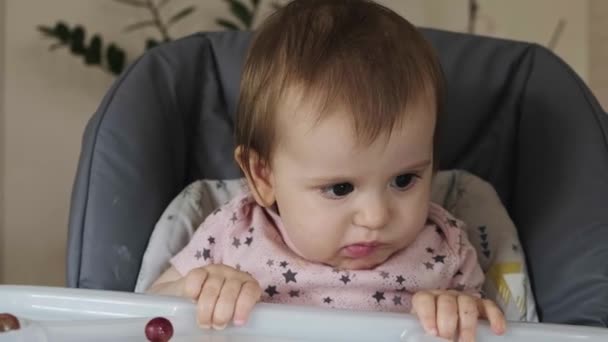 Video con una niña sentada en la mesa de bebé y comiendo grosella. Alimentos frescos y saludables. — Vídeos de Stock