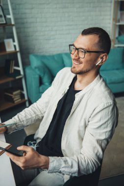 Elinde akıllı bir telefonla üniversitede öğrenim görürken not defterine notlar yazan bir adamın yan görüntüsü. İnternet teknolojisi. Beyaz adam..