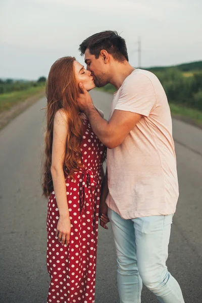 Vista lateral de um casal caucasiano em pé no meio da estrada beijando. Amor verdadeiro. — Fotografia de Stock