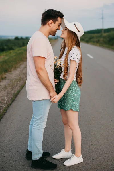 Um casal amoroso está de pé no meio da estrada de viagem, de mãos dadas e olhando um para o outro. Férias. Estilo de vida moderno. — Fotografia de Stock