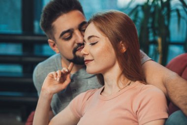 Doğum gününü kutlayan genç bir çiftin yakın plan portresi. Evdeki bir kanepede oturup öpüşüp kucaklaşıyorlar. Sevgiyle.