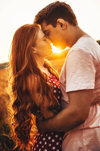 Side view of a woman with long red hair kissing her husband at an outdoor meeting. Posing against the bright background — Stock Photo, Image