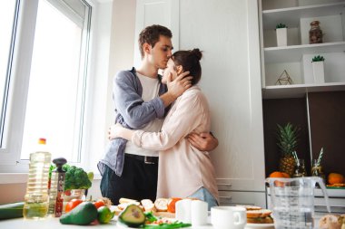 Kahvaltı hazırlıklarını bitirdikten sonra mutfakta kucaklaşan bir çift. Bir adam kadını alnından öpüyor. Sağlıklı bir yaşam tarzı. Vejetaryen sağlıklı yiyecekler. Sağlıklı