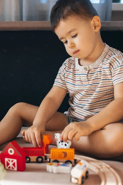 Menino caucasiano construindo trilhos ferroviários sentados no chão em casa. Brinquedos educativos para crianças. — Fotografia de Stock
