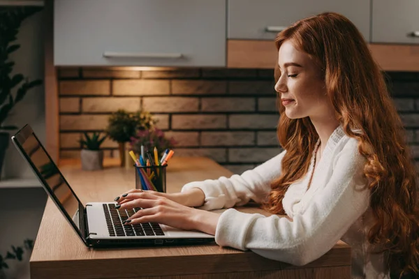 Kızıl saçlı bir iş kadınının salgın sırasında bilgisayarı uzak mesafe çalışması için kullanışının yan görüntüsü. Modern ofis içi. İnternet teknolojisi. Çevrimiçi — Stok fotoğraf