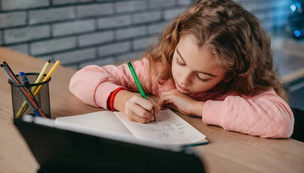 Colegiala haciendo su tarea usando tableta digital en casa. Educación a distancia. Chica estudiando en línea. Educación en línea moderna. —  Fotos de Stock