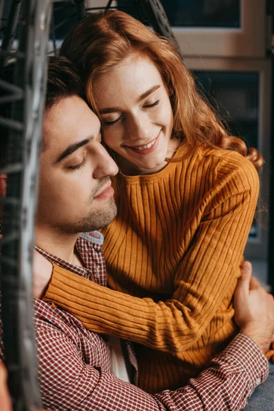 Closeup view of a loving couple embracing while sitting in big cozy chair at home. Red haired woman. Happy face. — Stock Photo, Image