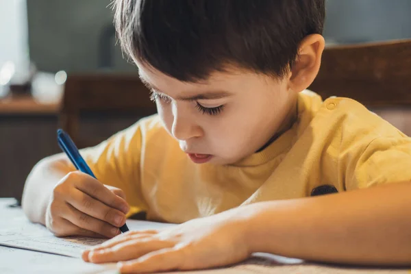 Retrato de cerca de un chico caucásico sentado en una mesa y escribiendo su tarea. Estudiar, hacer los deberes. —  Fotos de Stock