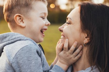 Doğada oğlunu kollarına alan mutlu bir annenin yan görünüş portresi. Yaşam tarzı tasarımı için portre. Aile günü. Dışarıda eğlence..