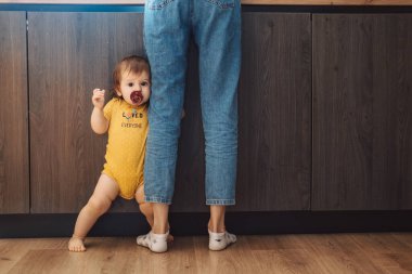 Evde annesinin bacaklarını tutan bir kızın portresi. Bebek bakımı.